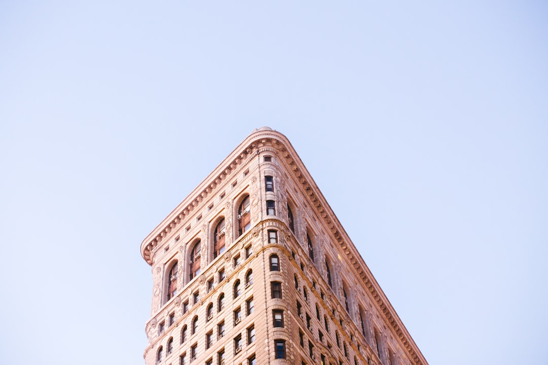 Flatiron building, New York City, soft pastel colors, minimalist photography, lowangle shot, captured by Sony Alpha A7 III camera with f/8 aperture setting and natural light, perspective, blue sky background, focusing on the architecture’s unique shape. –ar 128:85