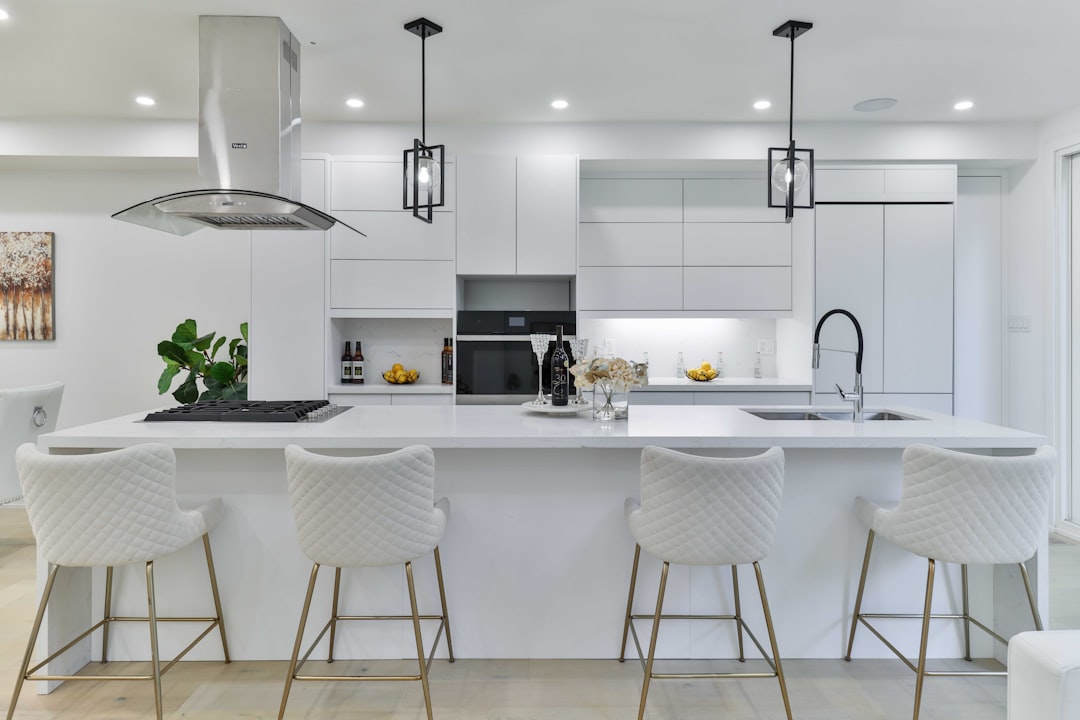 White modern kitchen with island, white cabinets and lighting, black pendant lights, barstools in the middle of an open space living room. The background is a bright studio. Shot in the style of Canon EOS R5 at F2, ISO30. –ar 128:85