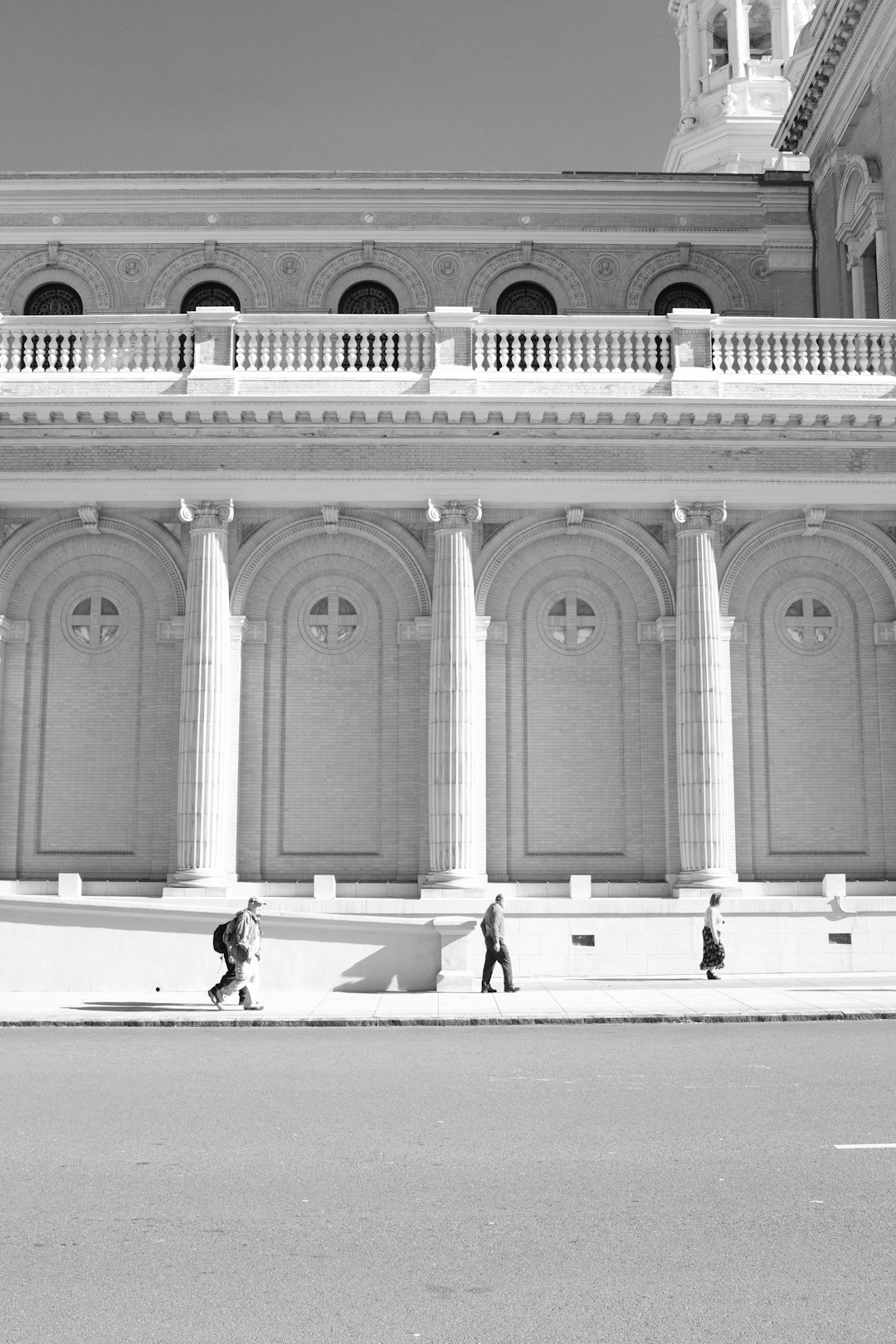 Black and white street photography of the suburban city hall in San Francisco, photographed in the style of Vivianne Sassen and [Brigitte Lacombe](https://goo.gl/search?artist%20Brigitte%20Lacombe), with soft light and high key lighting, showing 3 people walking around the building with big columns, in an architectural photography wide shot.