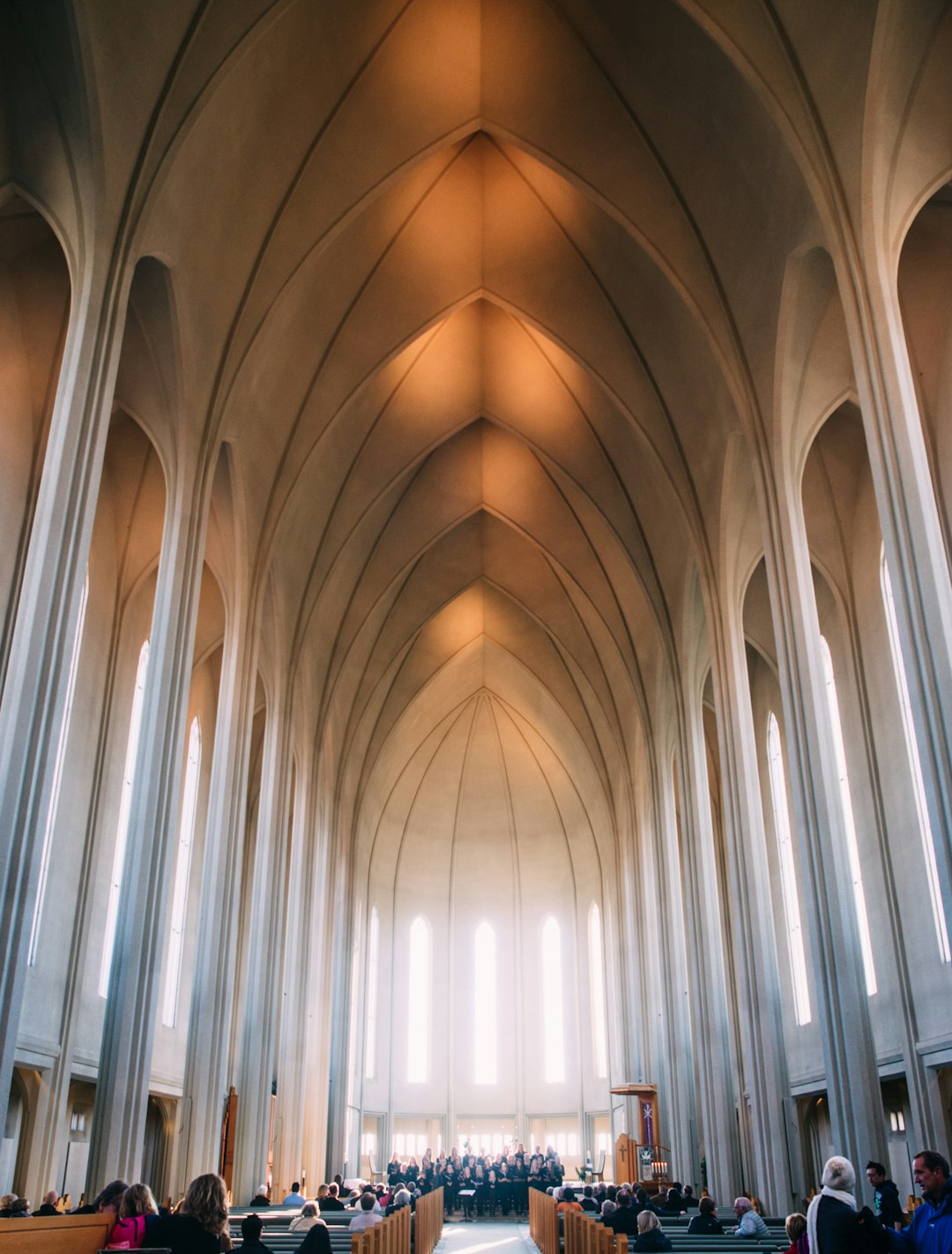 Icelandic church wedding, interior shot of the Hallgrímskirkja in the style of post modern architecture in Iceland, tall vaulted ceiling with large arched windows, people sitting on pews at their seats, photography, natural light, high resolution.