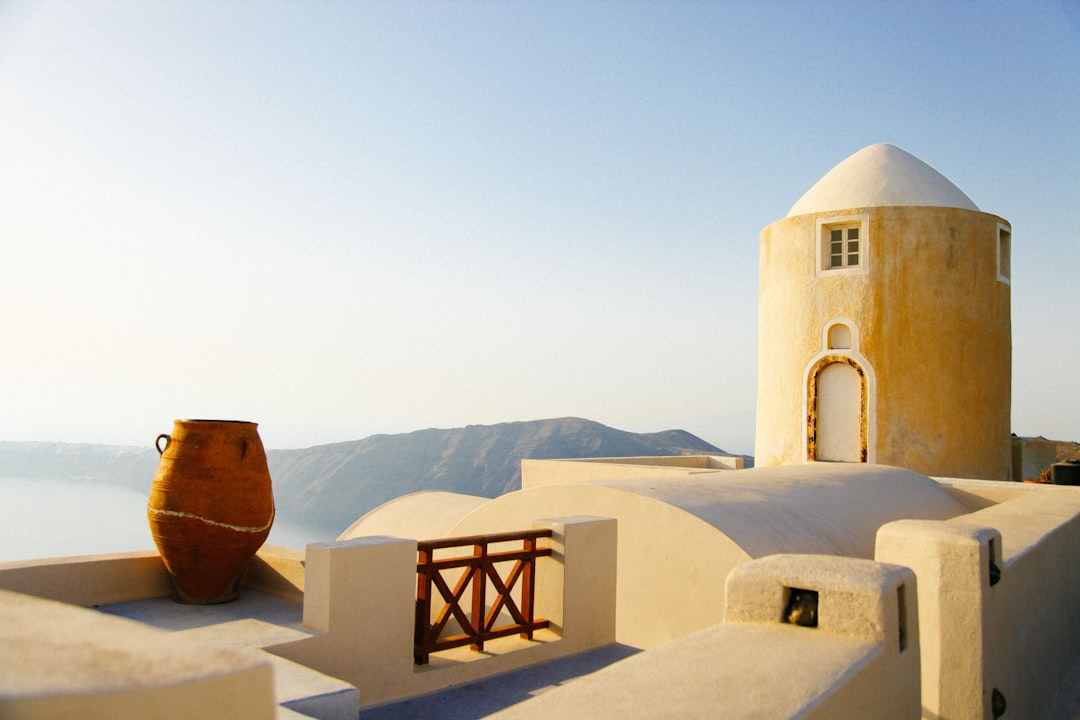 Stunning rooftop view of Santorini, with an old yellow pot and white walls, overlooking the sea. A small round tower is on one side, with soft morning light. The scene is captured in high resolution using Kodak Gold 400 film stock, showcasing every detail from the sky to the distant mountains. –ar 128:85