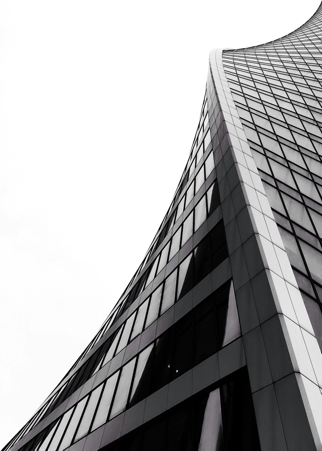 A tall curved building on a white background in a high contrast, wide angle, low angle shot architectural photography in the style of monochrome with black and grey tones featuring a skyscraper cityscape in an architectural style with glass windows and geometric shapes in an urban setting. –ar 91:128