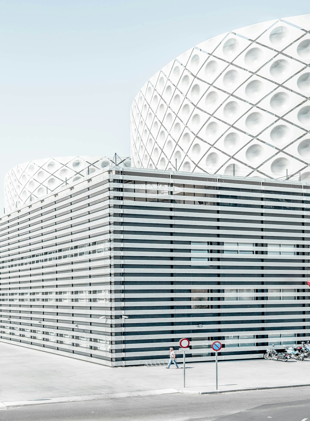 frontal photography of the facade of the scandinavian stadium building in the style of [Bjarke Ingels](https://goo.gl/search?artist%20Bjarke%20Ingels) with vertical slats in white color, in a pattern like criss cross or octagon shapes, located on a side street, clear sky, soft daylight