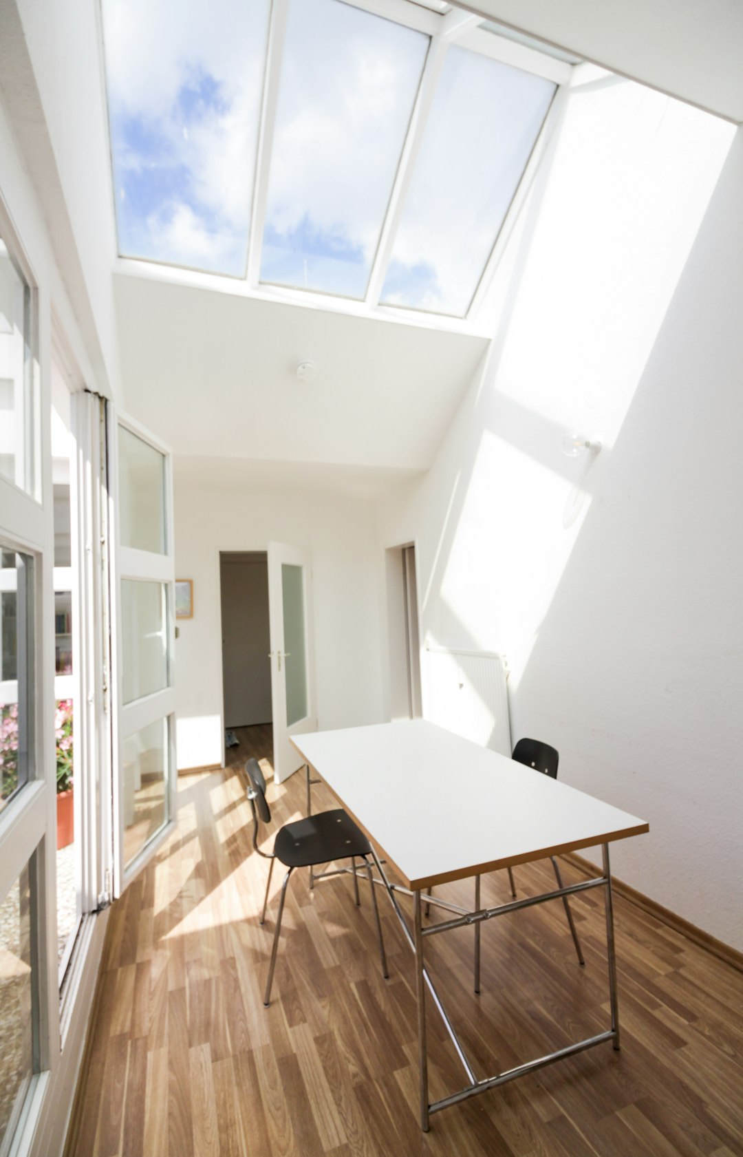 A small white table with black chairs in the center of an open room, skylights on top and a wooden floor, interior design photography with light sky blue window frames in the style of modern architecture.