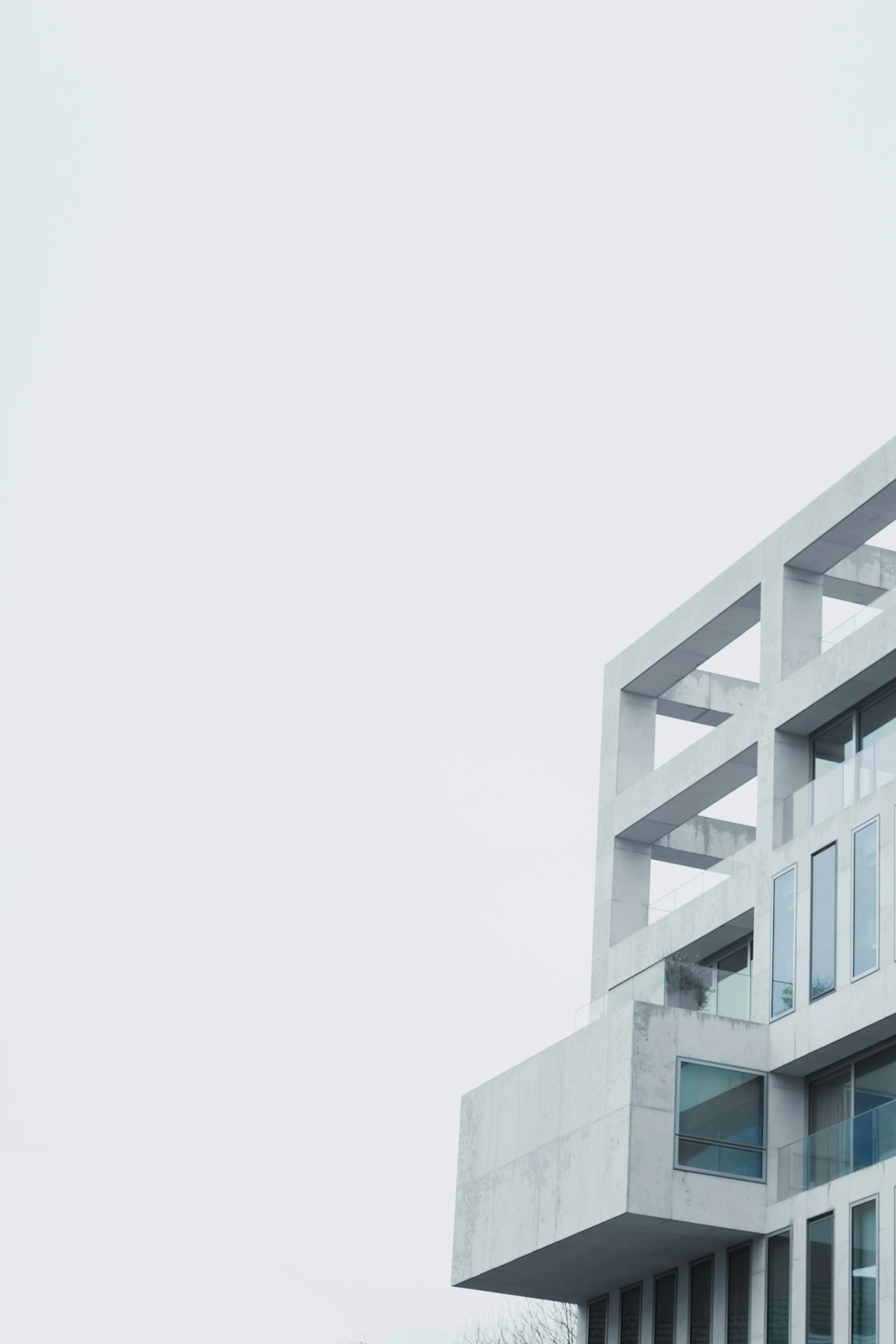 A white building with an angular design made of concrete, featuring rectangular windows and large balconies, set against the backdrop of a light grey sky. The focus is capturing details like textures in the structure’s surface, creating contrast between it and its surroundings. This photograph highlights modern architecture elements and adds depth to the composition. Shot in the style of photographer [Alex Strohl](https://goo.gl/search?artist%20Alex%20Strohl). Conceptual photography. Minimalistic architecture. White building. Textured concrete facade. Small balcony. Wide angle shot. Daytime.