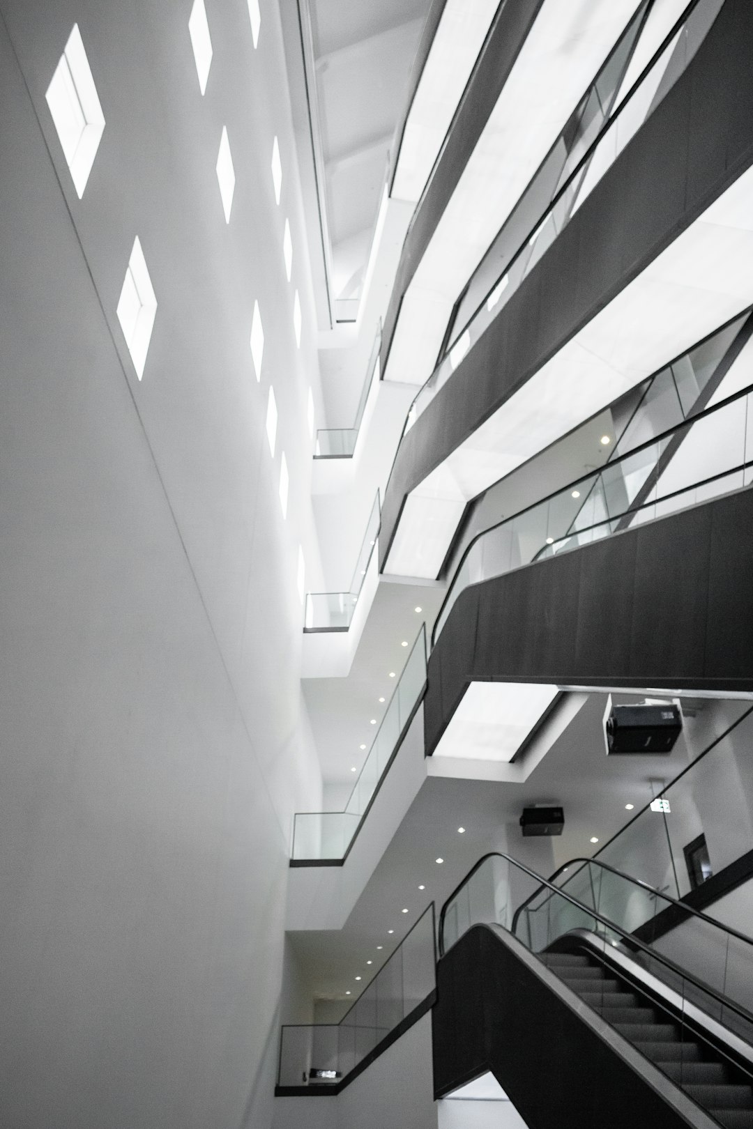 photography of the interior architecture of the modern museum, white walls with black details and glass, glass balcony railings, with three floors connected in the style of [Renzo Piano](https://goo.gl/search?artist%20Renzo%20Piano) connected to each other by bridges, there is an escalator going up in one corner of it, there’s light coming from above through windows on the ceiling and floor, some lights at ground level, natural lighting, wide angle shot, hasselblad camera –ar 85:128