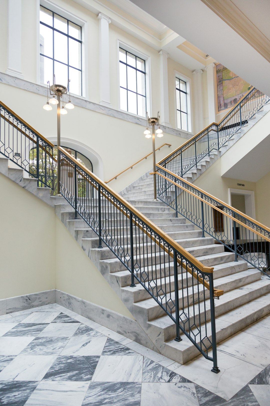 A wide staircase in the lobby of an American style school building, with marble steps and black metal railings leading to two floors above and below. The walls feature classical architecture elements and large windows, providing natural light for indoor lighting. A warm yellow ceiling adds warmth to the space. This scene is captured in the style of professional photographers using high-definition cameras and precise lenses.