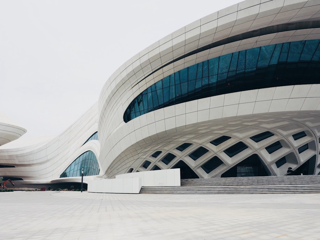 The exterior of the modern and futuristic arena features white walls with blue windows, designed in the style of [Zaha Hadid](https://goo.gl/search?artist%20Zaha%20Hadid) in Harbin’s square. front view, medium shot, symmetrical composition, architectural photography, 20mm lens –ar 4:3