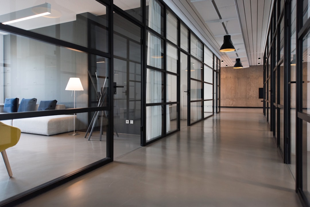 A photo of an office interior with black framed glass doors, leading to the open space where there is concrete flooring and a sofa area. The focus should be on one side wall that has large glass panels. There is also lighting in a yellow color. This scene will showcase how transparent glazing can create natural light while maintaining private spaces within the business environment.