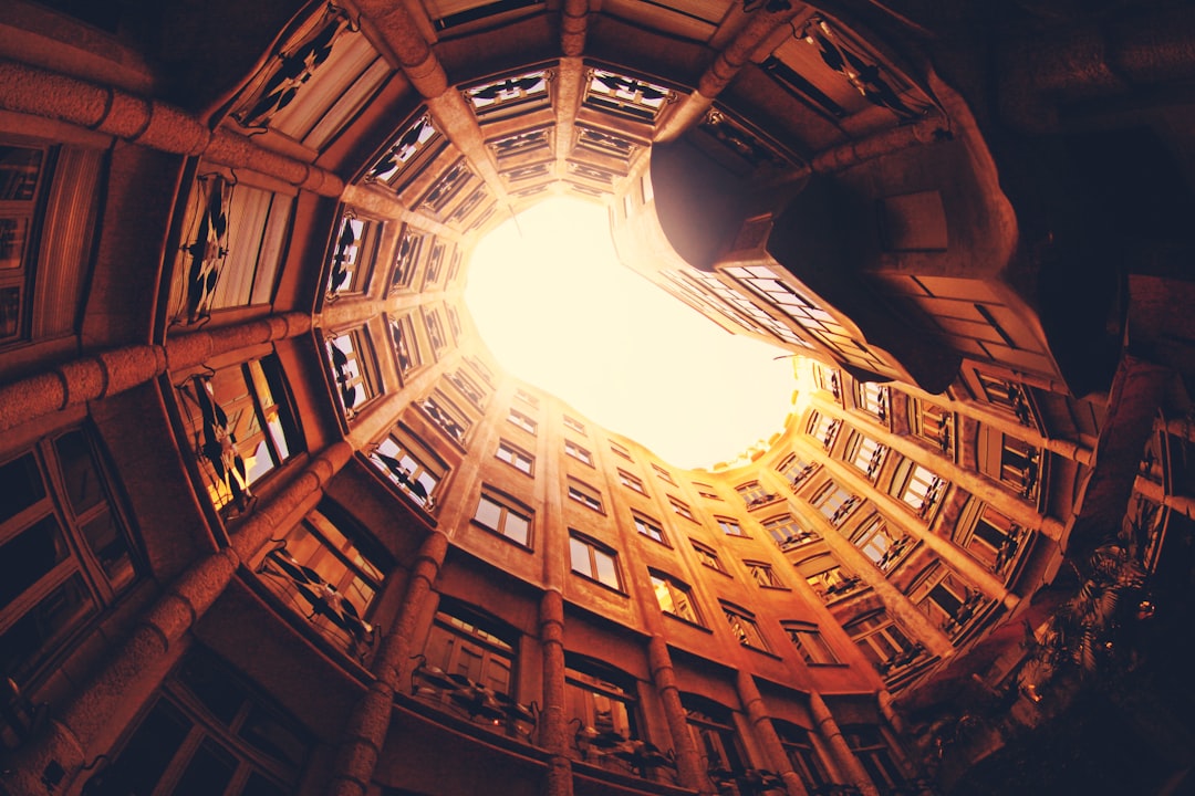 a fish eye view of the la remplazona building in barcelona, looking up at an open hole on top of one floor that is glowing with light from inside, warm tones, photography, –ar 128:85