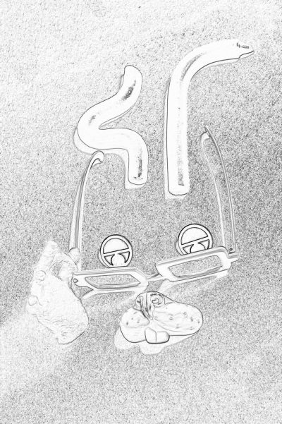 A pencil drawing depicts two pairs of eyeglasses with the letter "S" engraved on them, lying next to one pair and under another. The background is gray sand. White ink outlines form three eyes around each frame. A piece of fabric lies in between the glasses. Done in the style of a sketchy drawing.