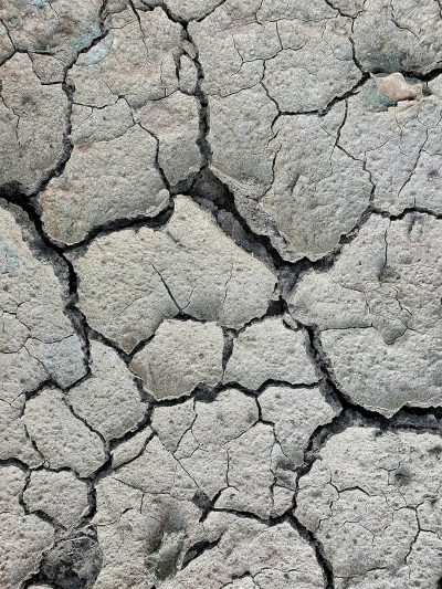 A close-up texture of cracked earth, symbolizing the harsh environment and dry weather conditions in arid areas. The background is a greyish brown with visible cracks that resemble rugged terrain. It creates an atmosphere of desolation. This pattern can be used as a digital backdrop for images or text in high resolution, in the style of office space. --ar 3:4