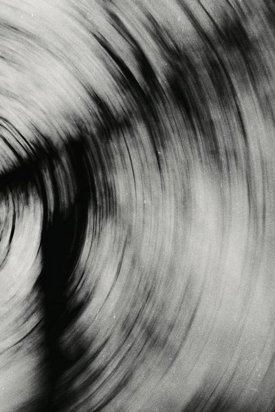 Abstract black and white photograph of an old vinyl record spinning, grainy texture, blurred motion, slow shutter speed, monochromatic tones with shades of gray and charcoal, focus on the vint circular patterns created by rotating grooves, creating visual effects reminiscent of wind and water ripples. The background is blurred to emphasize these intricate designs, evoking nostalgic memories or capturing the essence of music in mid tromp --ar 85:128