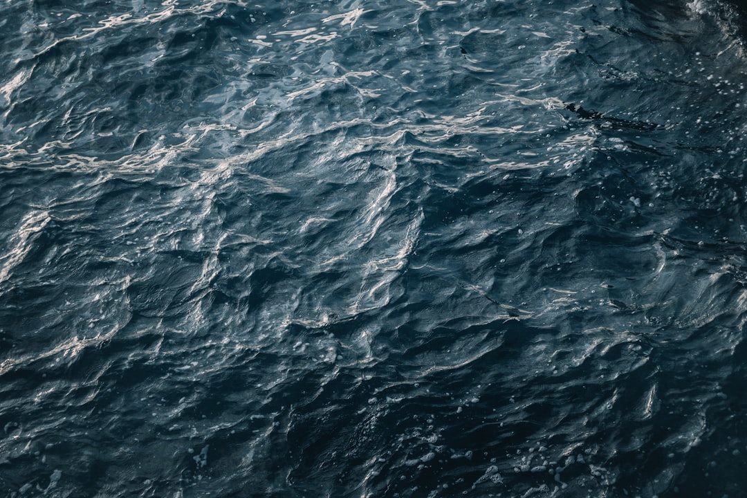 A topdown view of the dark blue sea, capturing its intricate patterns and textures with high detail. The water’s surface reflects light, creating ripples that highlight the depth below. Shot in the style of National Geographic photography, using Canon EOS R5 for sharpness and clarity. –ar 128:85