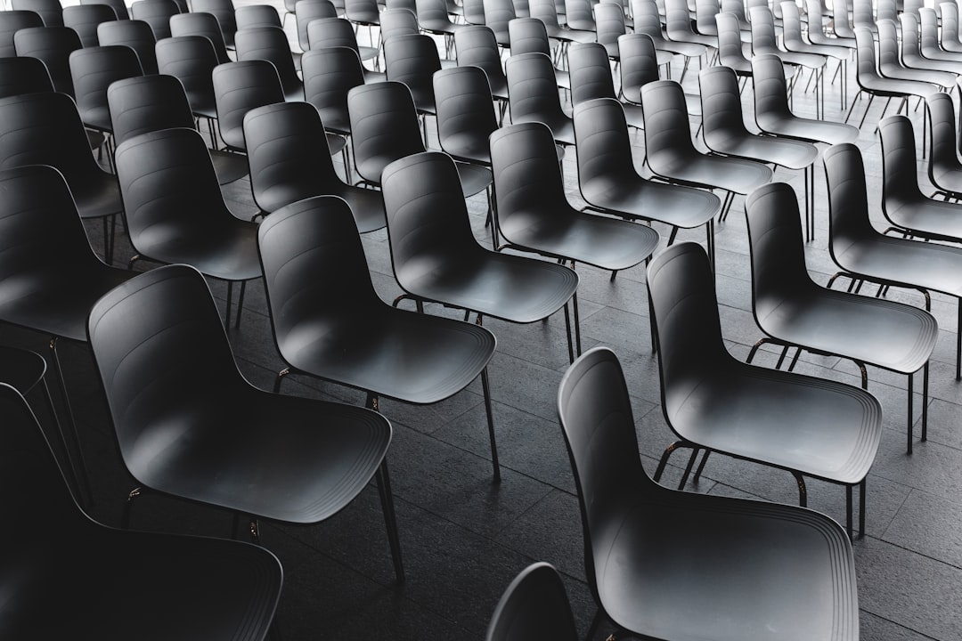 A large group of modern chairs were arranged in rows on the floor in a symmetrical composition. The high resolution photography had a minimalist style with cinematic lighting. A dark grey background was used with a closeup shot that showed the detailed texture. A monochrome color scheme created a balanced and harmonious layout. –ar 128:85