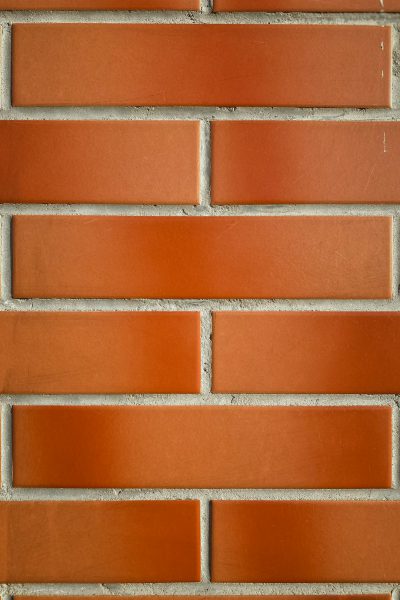 A closeup of an orange brick wall, with each row featuring three horizontal bricks in the same color and shape. The background is plain white to highlight the texture and pattern of the red brick surface. This photograph highlights one of the classic materials used for construction or interior design, with the style resembling a minimalist photograph. --ar 85:128