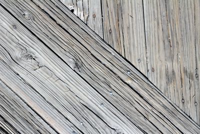 A closeup of an old, weathered wooden boardwalk with diagonal lines and visible wood grain texture. The background is a soft grey color to create depth in the composition. --ar 128:85