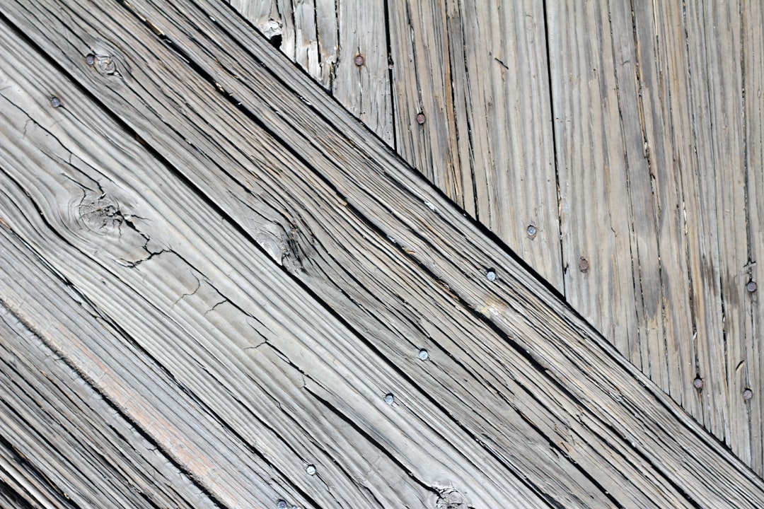 A closeup of an old, weathered wooden boardwalk with diagonal lines and visible wood grain texture. The background is a soft grey color to create depth in the composition. –ar 128:85