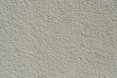 A closeup of the texture on an exterior wall, featuring a light gray stucco surface with visible roughness and fine particles in it. The background is neutral to highlight the detailed pattern of the concrete in the style of the concrete. --ar 128:85