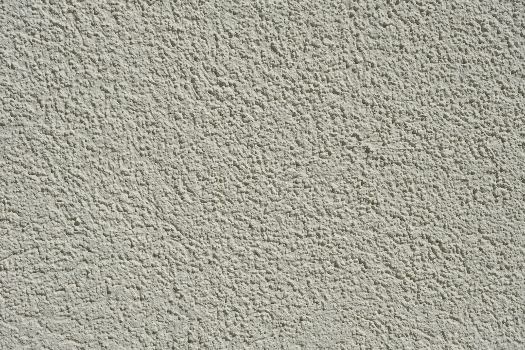 A closeup of the texture on an exterior wall, featuring a light gray stucco surface with visible roughness and fine particles in it. The background is neutral to highlight the detailed pattern of the concrete in the style of the concrete. –ar 128:85