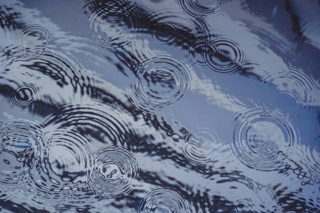 Raindrops creating circular ripples on the water surface, making abstract patterns and reflections in the sky. –ar 128:85