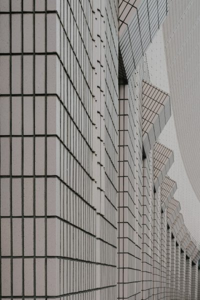 A closeup photo of the exterior wall texture of an art museum designed in the style of [Tadao Ando](https://goo.gl/search?artist%20Tadao%20Ando), featuring geometric grid lines on white tile walls and the abstract shape of arches on concrete walls. The background is a modern urban landscape with contemporary architecture. The lighting casts soft shadows over the textured surface, creating depth in both space and structure. --ar 85:128