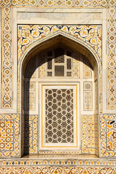 An arch in the wall of an ancient palace, with intricate geometric patterns and motifs on white marble accented with yellow and orange, intricate designs, arabesque patterns, arched doorways in the style of Indian architecture, a window frame in the center of the composition, photography. --ar 85:128