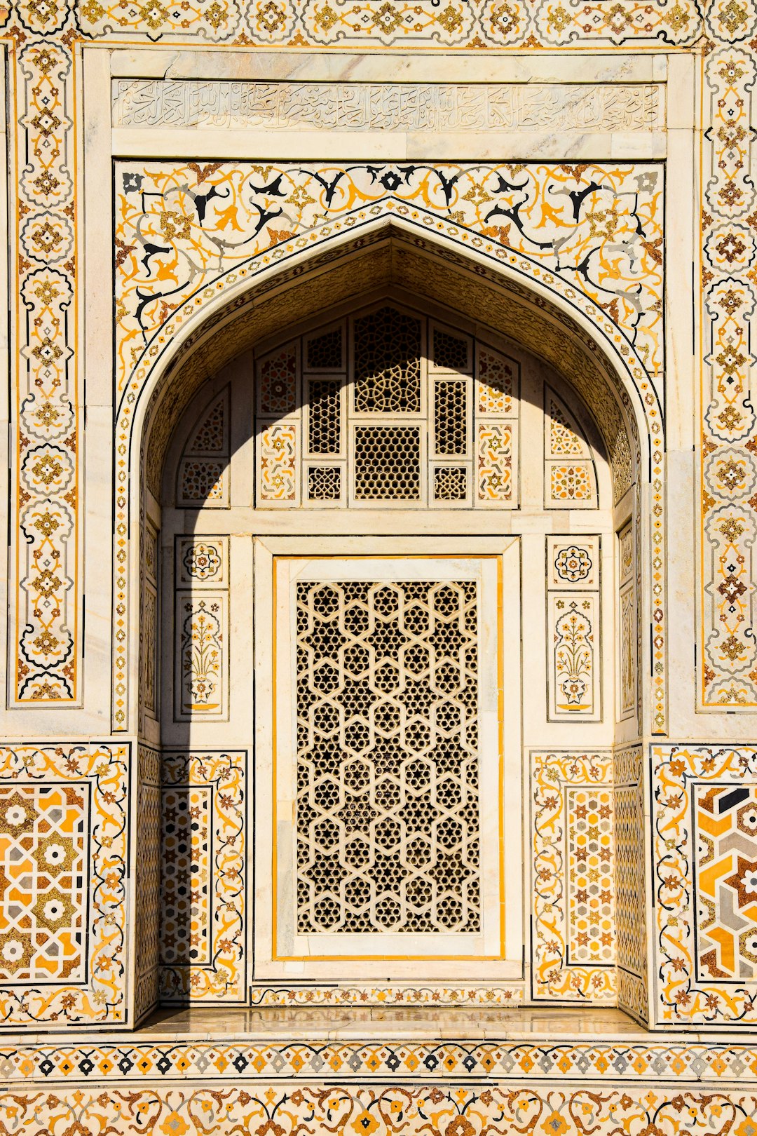 An arch in the wall of an ancient palace, with intricate geometric patterns and motifs on white marble accented with yellow and orange, intricate designs, arabesque patterns, arched doorways in the style of Indian architecture, a window frame in the center of the composition, photography. –ar 85:128