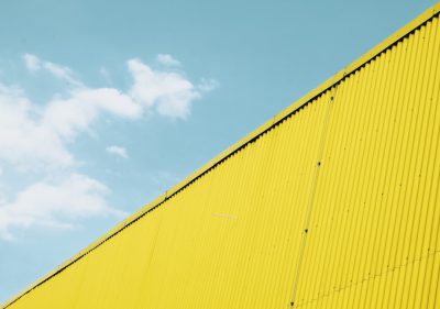 A yellow wall of an industrial building with the sky in the background, closeup, minimalism, high resolution photography, minimalistic style, low angle shot, bold color contrast, summer mood, daylight --ar 64:45