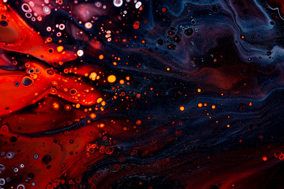 A closeup of swirling red and blue acrylic paint, with bubbles forming in the liquid. The background is dark and moody, adding to the mysterious atmosphere. –ar 128:85