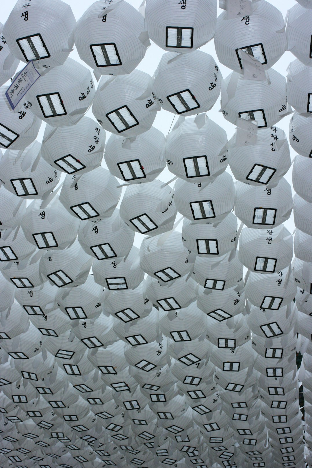 In the center of an outdoor square, white lanterns with black numbers hang from above to form large shapes. The ceiling is covered in paper balls that look like windows and doors. It’s a Chinese New Year celebration with Chinese style architecture and a Chinese culture theme park installation art made up of countless round rice dumpling shaped lanterns hanging upside down from top to bottom. in the style of Jeanแจ.trout, concept art, conceptual design, creative, innovative architecture. –ar 85:128