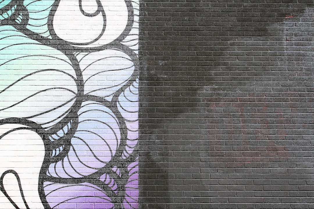 A simple, colorful graffiti design on the left side of an urban brick wall with black grout, featuring white and purple swirls on top of blue patterns, creating a contrast between lightness and shadowy areas. The background is a deep gray color, providing space for creative thinking or visualizing ideas. This art style could be used in street art projects to add depth and texture to city walls, adding a modern touch to traditional murals. –ar 128:85