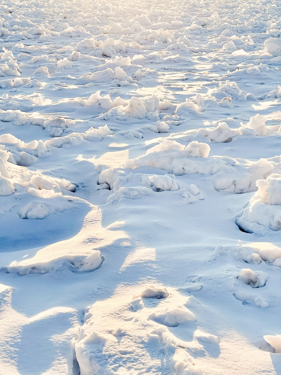 The vast expanse of white snow, covered with many large and small ice blocks scattered on the ground, shining in sunlight, in the style of photography, high definition. –ar 3:4