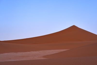 A large sand dune in the desert, the top of which is covered with fine red orange sand and white sand on one side. The sky above it has just turned blue. In front you can see another very small sand pile, which forms an S-shaped curve to give depth of field. This photo was taken in the style of Nikon camera, showing the vastness of the scenery. It's a real picture that makes me feel like I'm there! Nothing other than setting off alone into the Sahara Desert. --ar 128:85