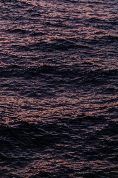 The surface of the dark sea, with some ripples on it, is a closeup shot of water at dusk. The water has soft tones and light purple reflections in high definition photography. In the distance, there were faint waves under the setting sun, creating an atmosphere full of mystery and tranquility. The photography has high contrast colors in a movie quality style. --ar 85:128