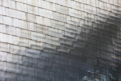 Photograph of the facade wall cladding made from gray metal shingles, with shadows and reflections in the style of the facade. --ar 128:85