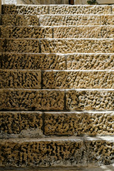 An old stone staircase with rough textures, aged stones and weathered surfaces in a closeup shot with warm tones and detailed textures, with an ancient city of Jerusalem background, photography. --ar 85:128