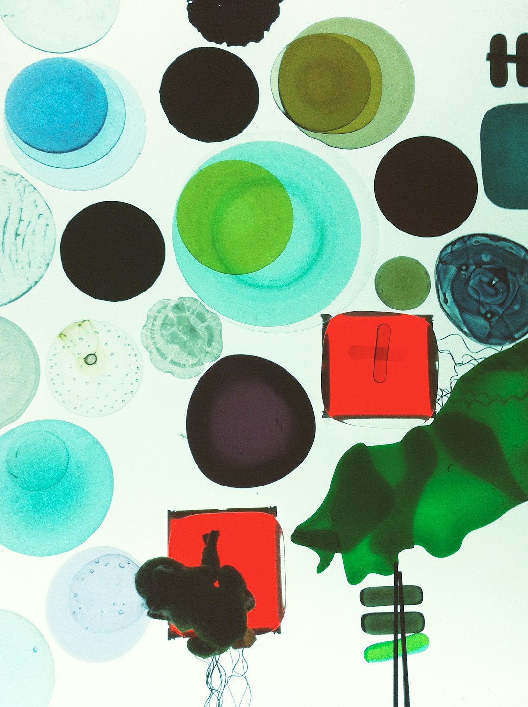 A white background with black, green and red circles of color representing cells floating in the center. The colors blend into each other, creating an abstract representation of cell structure. In one corner is a small figure holding up two pieces of glass that fit together perfectly to form another plate. This highlights minimalistic detail, and includes elements like wires connected between plates, indicating technological equipment used for study or experiment in the style of minimalism. –ar 95:128