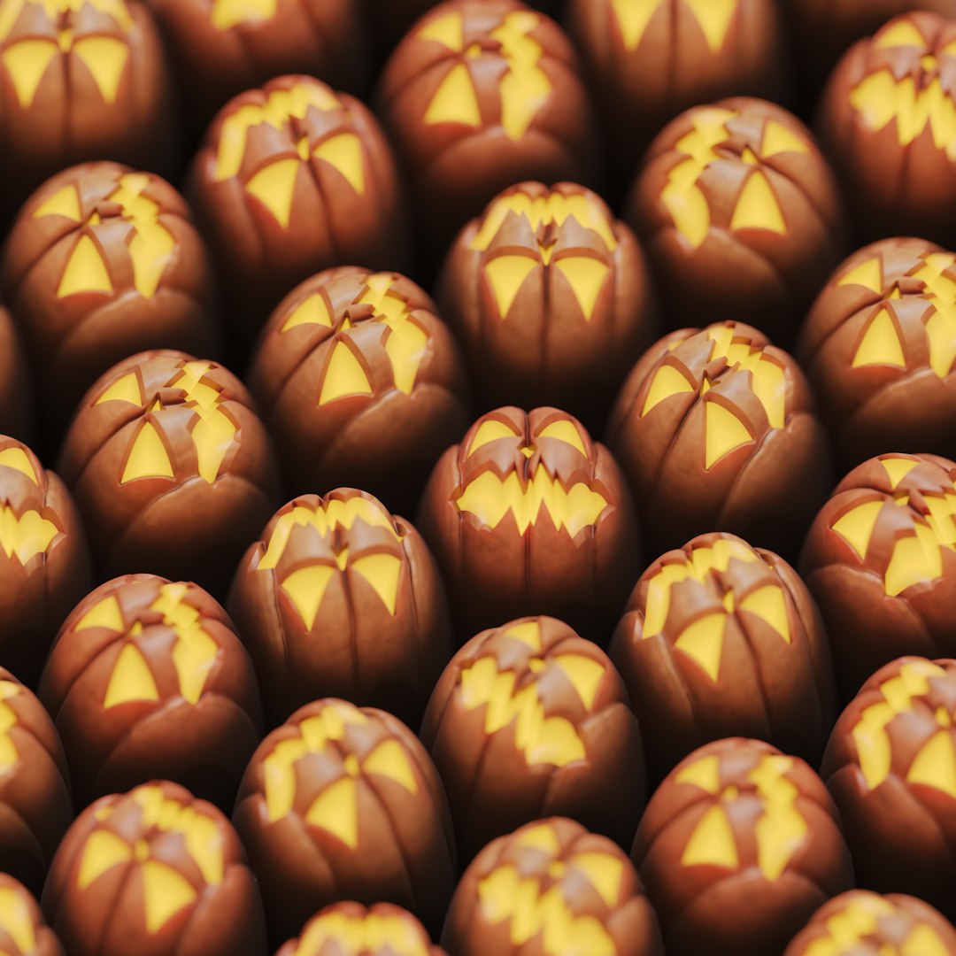 A pattern of chocolate pumpkins, each with yellow carved patterns on the top and a shiny surface. The pattern is arranged in rows and columns, creating an eye-catching display that would make for delightful confectionery treats. The focus is on facial expressions.