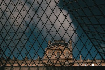 A photo of the Louvre Museum in Paris seen through glass with a cloudy sky and a dark blue color palette in the style of unsplash photography. --ar 128:85