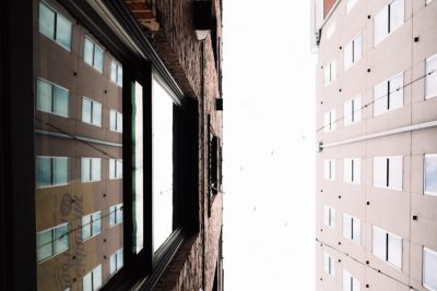 Looking up at the corner where two buildings meet, one window on each building is open and white sky can be seen through it, the photo taken with provia film in the style of unknown artist. --ar 128:85