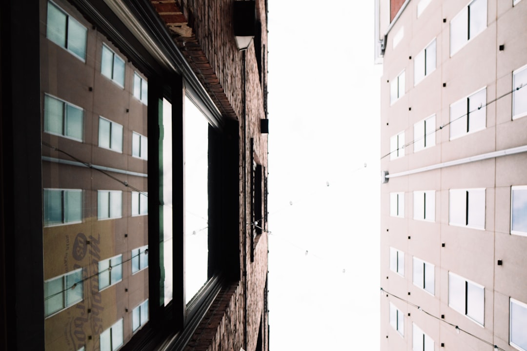 Looking up at the corner where two buildings meet, one window on each building is open and white sky can be seen through it, the photo taken with provia film in the style of unknown artist. –ar 128:85