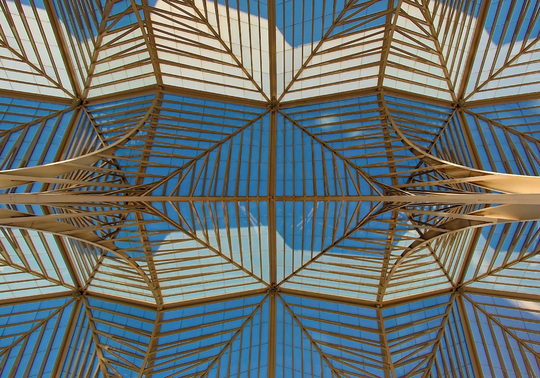 An architectural photograph of the roof structure of Las Stringas in the Tent, Lisbon. The skylight is made out of wood and glass. It has symmetrical geometric patterns that mirror each other. Use a Sony Alpha A7 III camera with an FE 24-85mm f/3.5 to 60 mm lens at F/9 aperture setting. Capture the architecture from below. Vibrant colors. High resolution. –ar 128:89