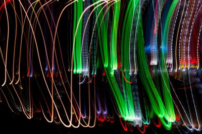 A long exposure photograph capturing the light trails of multiple colorful lights, creating an abstract and dynamic pattern against a black background. The colors dance across the screen in fluid lines, evoking movement and energy. This artistic representation is perfect for conveying vibrant, energetic themes or festive moments like Christmas, New Year's Eve, St Patrick’s Day, Easter, etc., isolated on white background --ar 128:85