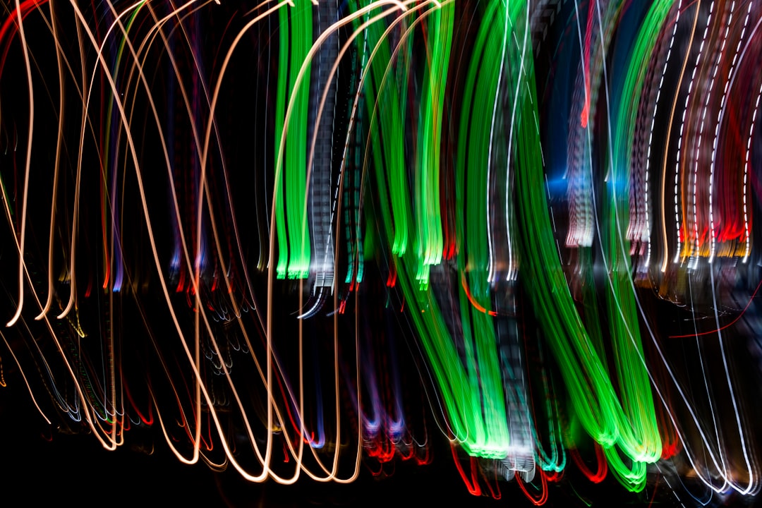 A long exposure photograph capturing the light trails of multiple colorful lights, creating an abstract and dynamic pattern against a black background. The colors dance across the screen in fluid lines, evoking movement and energy. This artistic representation is perfect for conveying vibrant, energetic themes or festive moments like Christmas, New Year’s Eve, St Patrick’s Day, Easter, etc., isolated on white background –ar 128:85