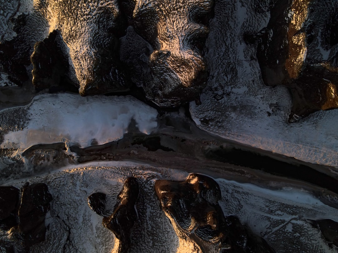 Aerial view of the dark rocks covered with snow and ice, illuminated by golden sunlight. The shadows cast on these rocks form unique patterns resembling animal heads. A small stream flows through it, adding to its natural beauty. Shot in high resolution using a Nikon D850 camera and an aperture setting of f/4, in the style of the photographer. –ar 4:3