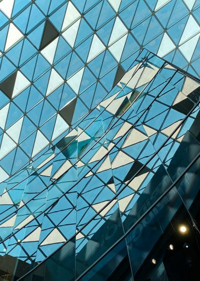 A photograph of the glass roof with triangular shapes, reflecting light and creating an illusionary effect in shades of blue against a clear sky background. The building's architecture is contemporary with geometric patterns on its exterior walls. This shot captures both the architectural details and natural lighting that highlights textures within each diamond shaped window in the style of contemporary geometric patterns. --ar 91:128