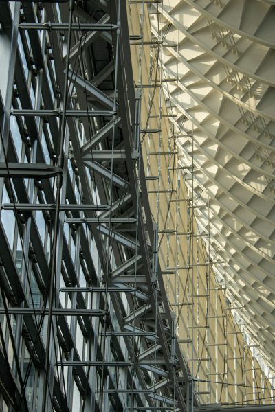 Organized steel structure, angular grid patterns, modern architecture with a glass roof and steel frame structure, surrounded by scaffolding for building work, light-colored interior walls and white ceiling, contrasting shadows from the window frames. High resolution photography, architectural photograph of an airport terminal designed in the style of [Zaha Hadid](https://goo.gl/search?artist%20Zaha%20Hadid), architectural photography. --ar 85:128