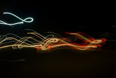 long exposure of light trails on black background, one line is white and the other red with gold highlights --ar 128:85