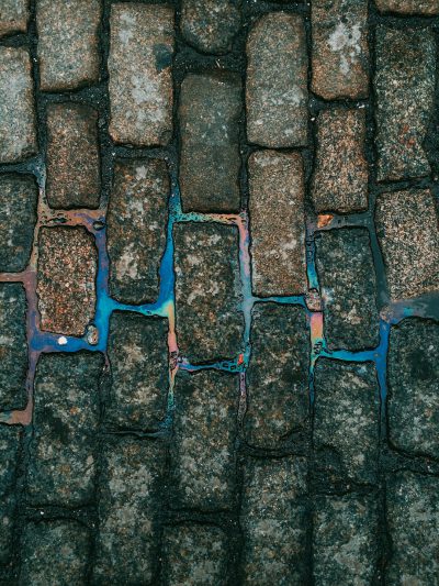 A photograph of a cobblestone street with blue and green oil stains, taken from a top view, with high resolution photography, insanely detailed fine details, isolated on a white background, a stock photo with professional color grading and an award winning composition, lit with cinematic lighting on an overcast day, photographed with a 35 mm lens at f20, in the style of a Canon EOS R6s Mark II. --ar 3:4